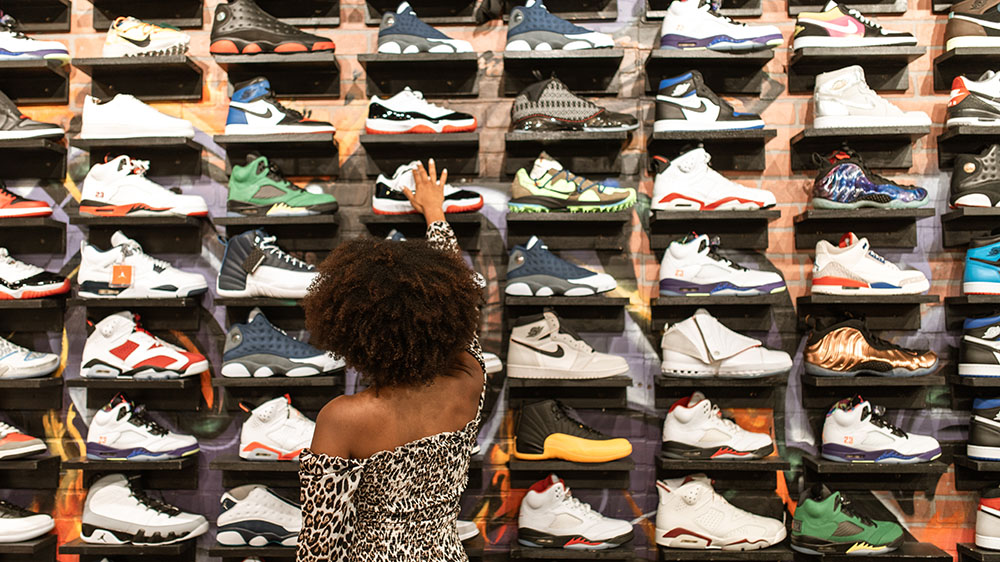 En kvinne strekker seg etter en sko i en butikkhylle full av joggesko