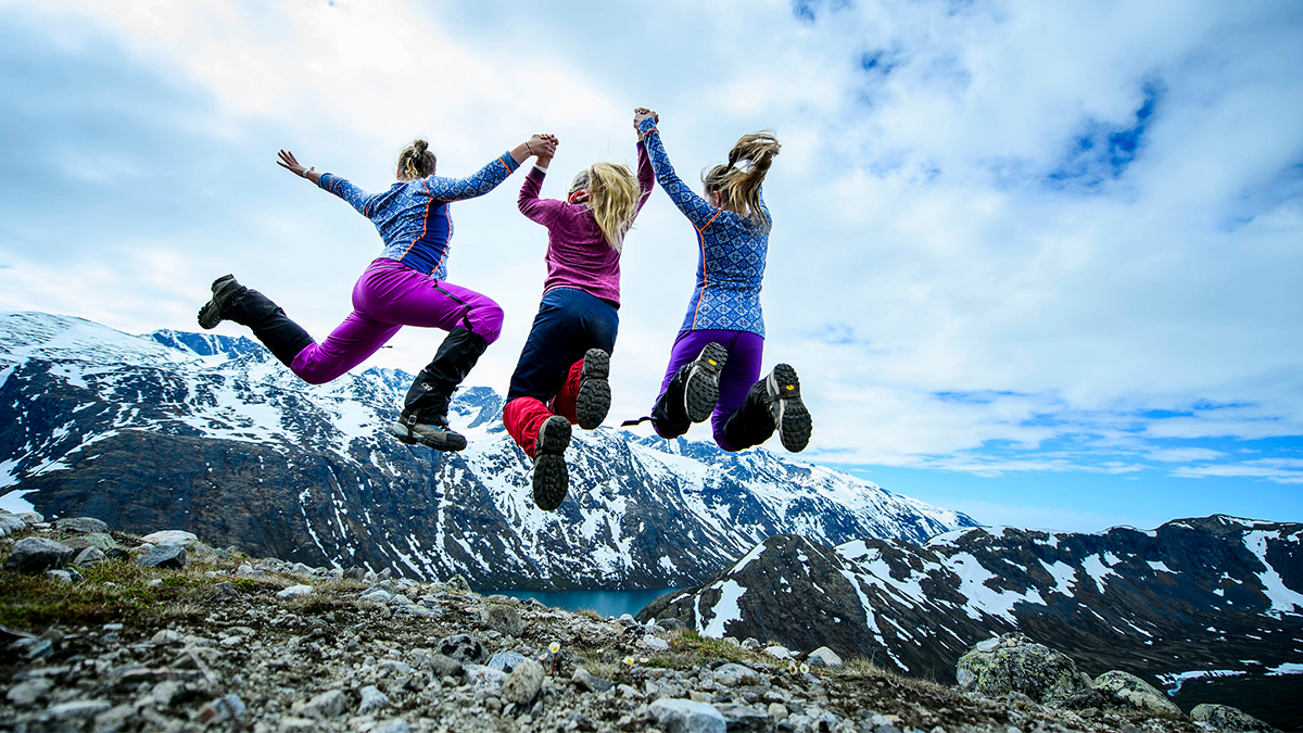 Three girls on a mountain hike make a jump.