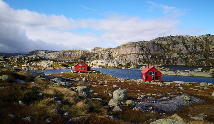 bildet av DNT Hytte i Sandvatn. Vann, fjell og rødmalte hytter