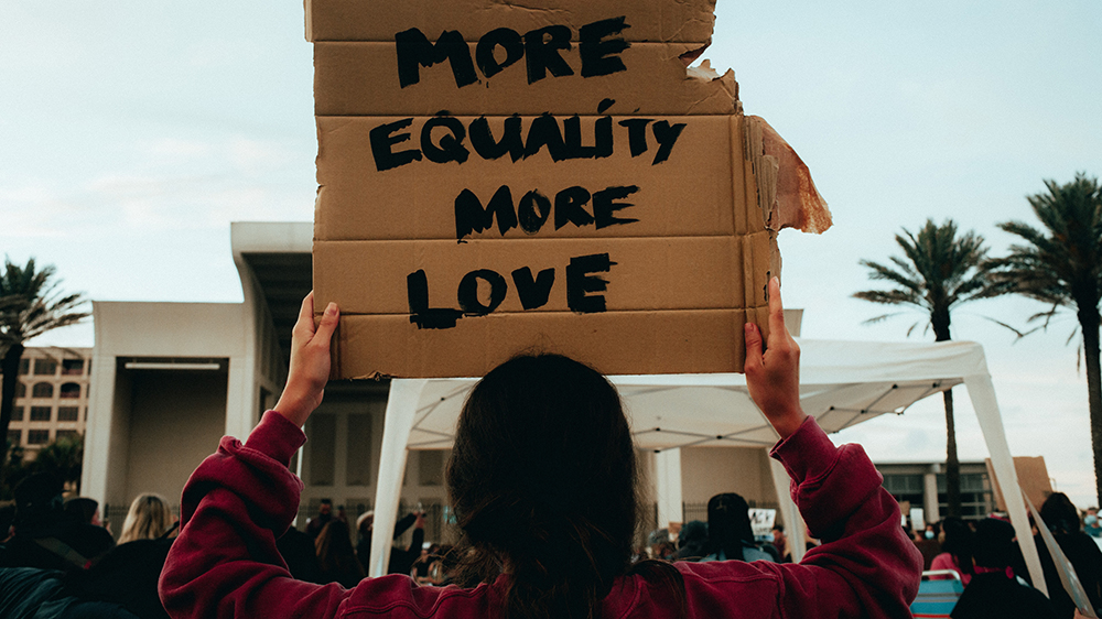 Demonstrant med plakat med teksten "MORE EQUALITY MORE LOVE"